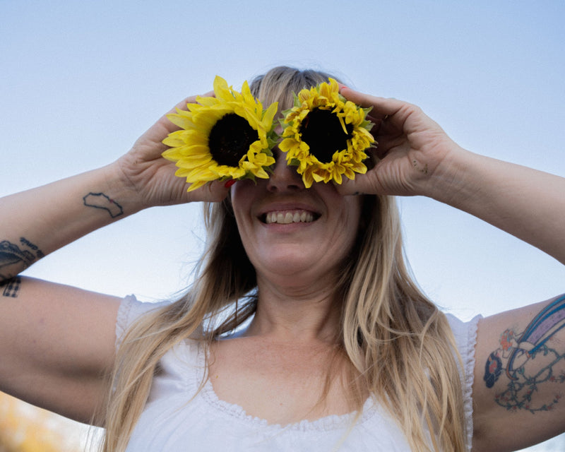Emily holding two sunflowers over her eyes like binoculars against a blue sky