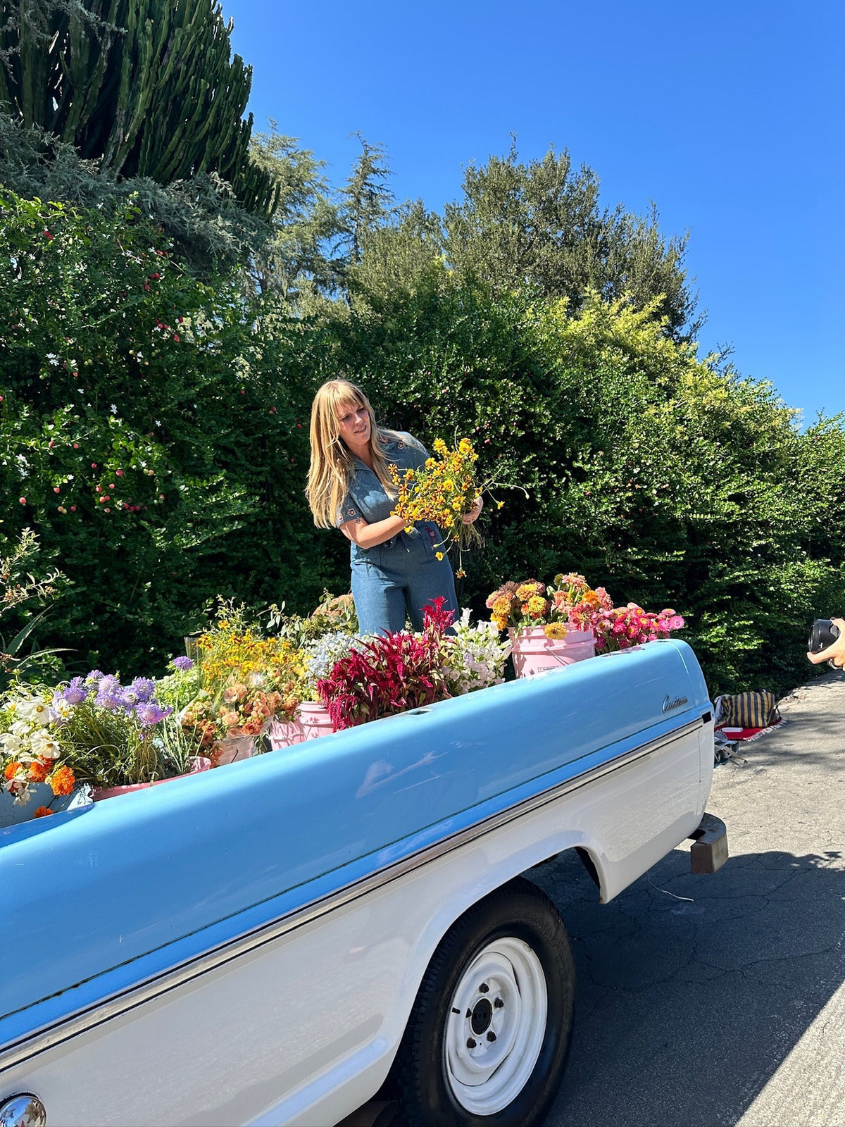 Emily arranging a bouquet in the bed of the baby-blue flower truck, filled with buckets of fresh flowers