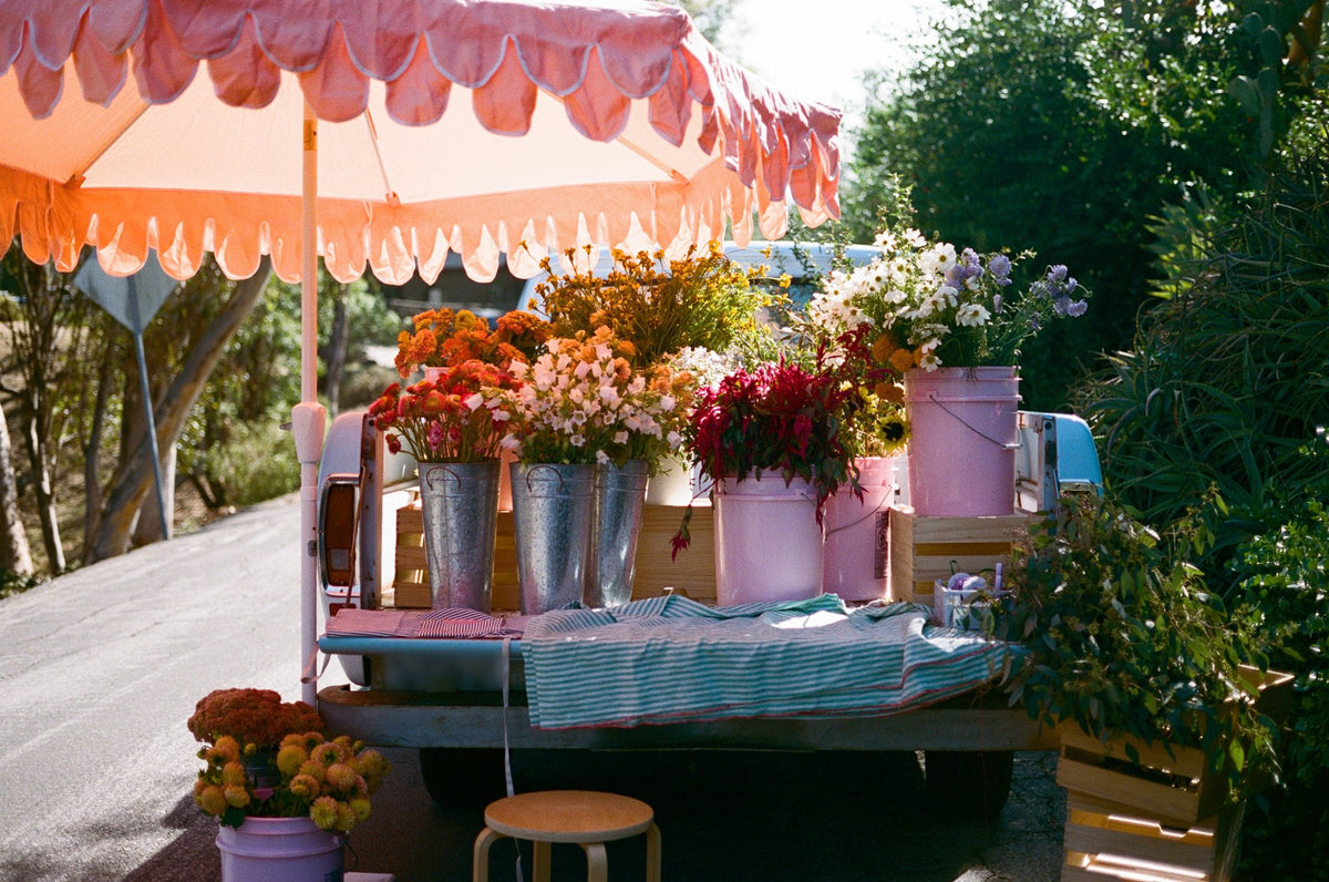 The Long Lost Buds bouquet bar set up on the tailgate of the baby-blue truck under a pink scalloped umbrella, with buckets of zinnias, celosia, cosmos and dahlias