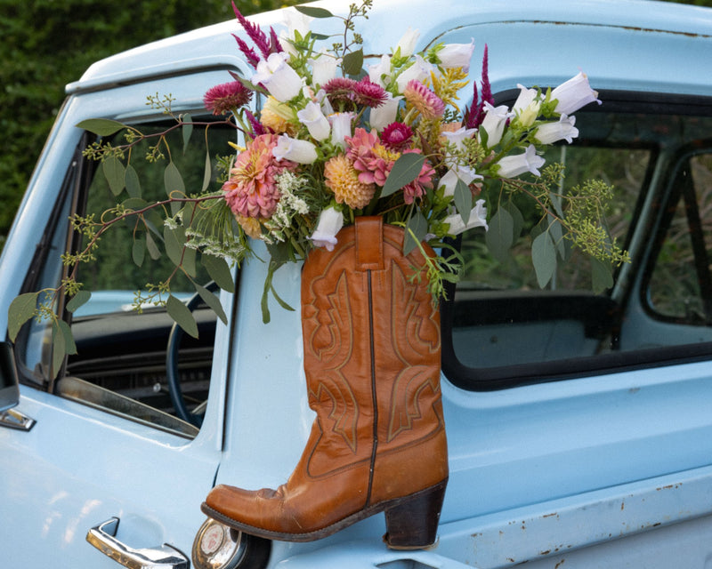 A bouquet of celosia, snapdragons and eucalyptus arranged in a cowboy boot hanging from the flower truck's window